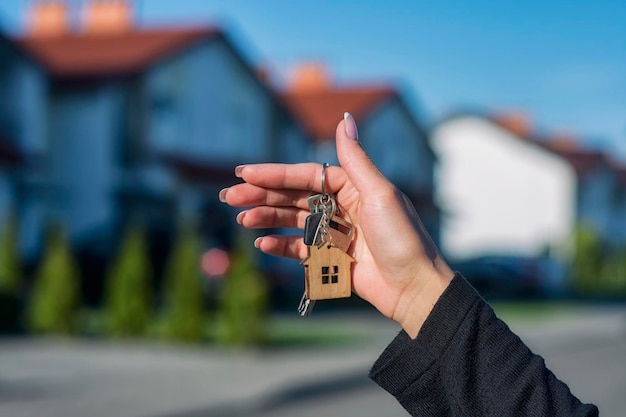 Een vrouw houdt de sleutels van het huis in haar handen tegen de achtergrond van woongebouwen Concept voor het kopen en huren van appartementen