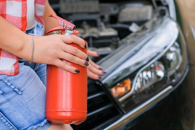 Een vrouw houdt een brandblusser in haar handen terwijl ze bij de open motorkap van een autoclose-up staat