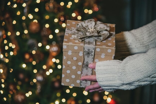 Een vrouw houdt een cadeautje voor een kerstboom.