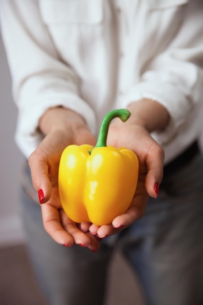 Een vrouw houdt een gele paprika in haar handen.
