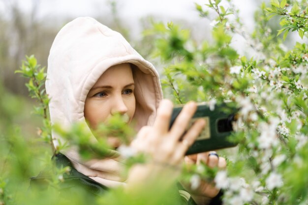 Een vrouw houdt een mobiele telefoon in haar handen en maakt foto's van planten