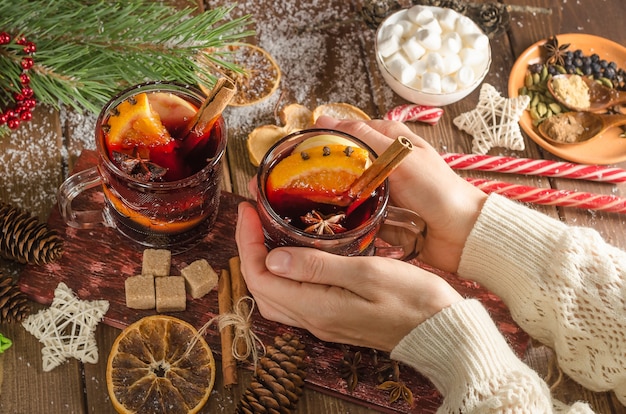 Een vrouw houdt een mok glühwein met een schijfje sinaasappel op een houten achtergrond. donkere stijl