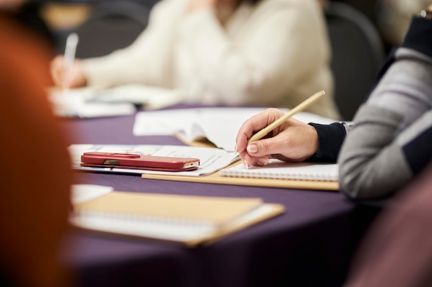 een vrouw houdt een pen in haar hand, maakt aantekeningen tijdens een conferentie in een notitieboekje.