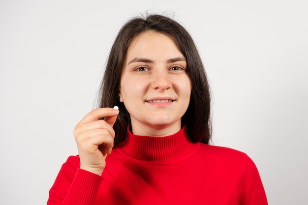 Een vrouw houdt een pil in haar hand op een witte achtergrond