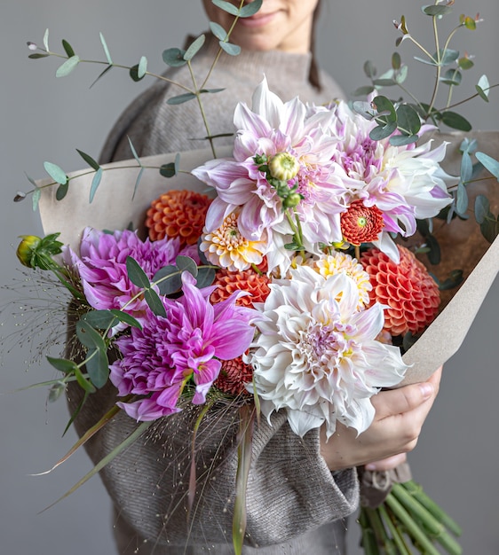 Een vrouw houdt in haar handen een groot feestelijk boeket met chrysanten en andere bloemen, close-up.