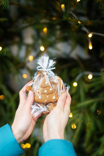 Een vrouw houdt in haar handen peperkoek in de vorm van een kerstboom op de achtergrond van een groene kerstboom buitenshuis Het concept van wintervakanties, snoep en gezelligheid