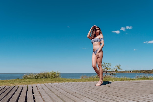 Een vrouw in bikini staat op een promenade voor een watermassa.