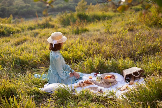 Een vrouw in blauwe jurk zit op een picknick in een park met panoramisch uitzicht