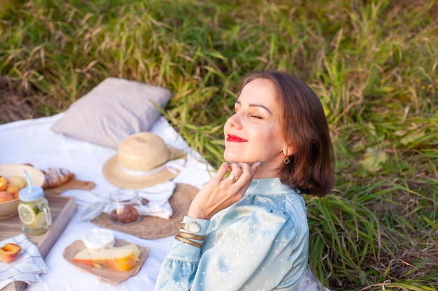 Een vrouw in blauwe jurk zit op een picknick in een park met panoramisch uitzicht