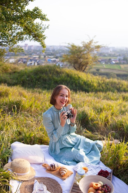 Een vrouw in blauwe jurk zit op een picknick in een park met panoramisch uitzicht