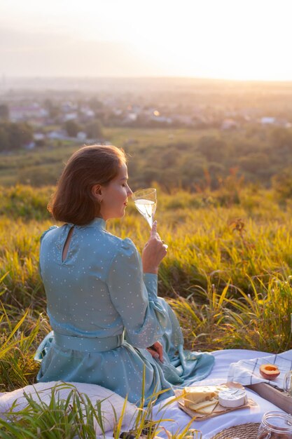 Een vrouw in blauwe jurk zit op een picknick in een park met panoramisch uitzicht