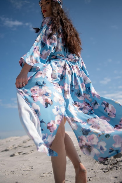 Een vrouw in een blauwe bloemenjurk loopt over het strand.