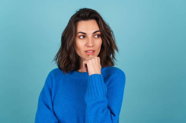 Een vrouw in een blauwe gebreide trui en natuurlijke make-up, kort krullend haar, kijkt bedachtzaam weg en denkt na over ideeën