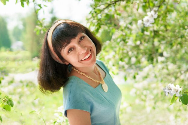 Een vrouw in een blauwe jurk onder een bloeiende boom in de tuin in het voorjaar. De brunette lacht en is blij