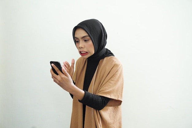 Een vrouw in een bruine jas houdt een telefoon vast en kijkt naar haar gezicht.