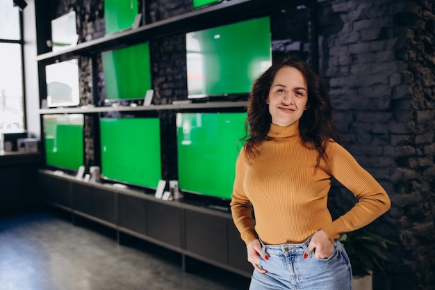 Een vrouw in een elektronicawinkel kiest een tv op de achtergrond van tv's met een groen scherm