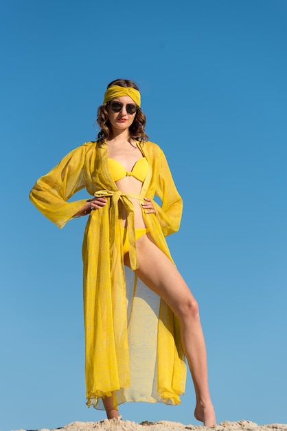 Een vrouw in een geel zwempak staat voor een blauwe lucht.