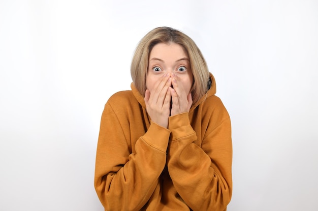 Een vrouw in een gele hoodie bedekt haar mond met haar handen