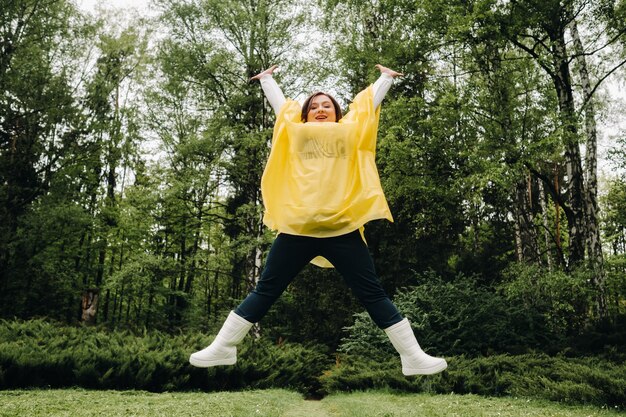 Een vrouw in een gele regenjas toont emotie en stuitert in de zomer voor de regen door het park.