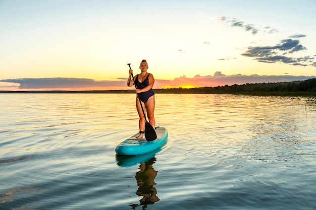 Foto een vrouw in een geschoren badpak met een hanenkam op een supboard bij zonsondergang in het water