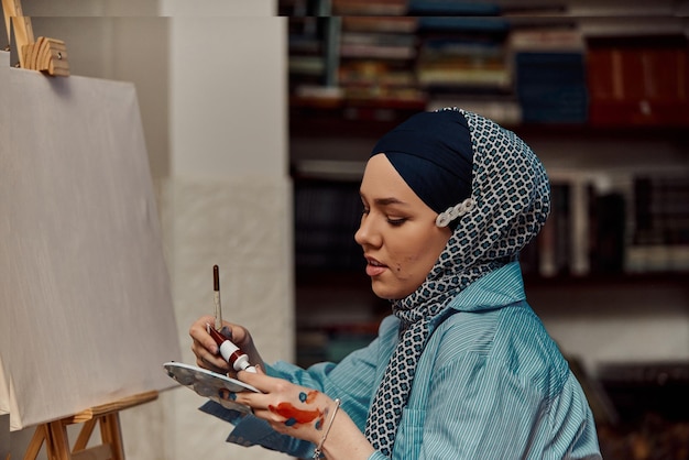 Een vrouw in een hijab schildert op canvas met een penseel en tempera