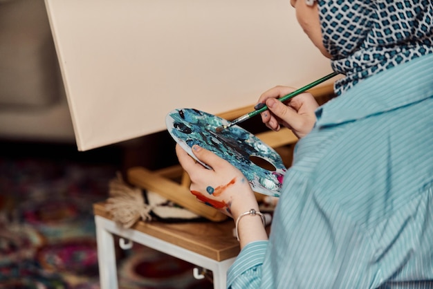 Een vrouw in een hijab schildert op canvas met een penseel en tempera