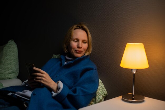 Een vrouw in een jas ligt op het bed met een telefoon in haar handen Communicatie per telefoon via sms Tijd doorbrengen op sociale netwerken