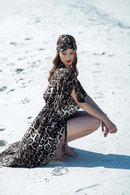 Een vrouw in een jurk met luipaardprint poseert op het strand.