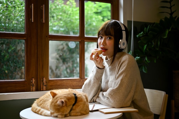 Een vrouw in een knusse trui die naar muziek luistert en donuts eet en aan een tafel zit