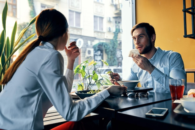 Een vrouw in een licht overhemd en een zakenman lunchen aan een tafel in een café, heerlijk eten, drinken medewerkers