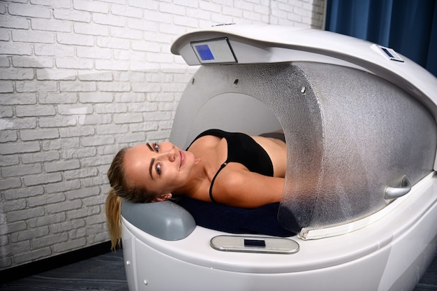 Foto een vrouw in een moderne spa-capsule en die professionele niet-invasieve gewichtsverlies, anti-cellulitis en verjongende schoonheidsbehandeling krijgt in het wellness-spacentrum