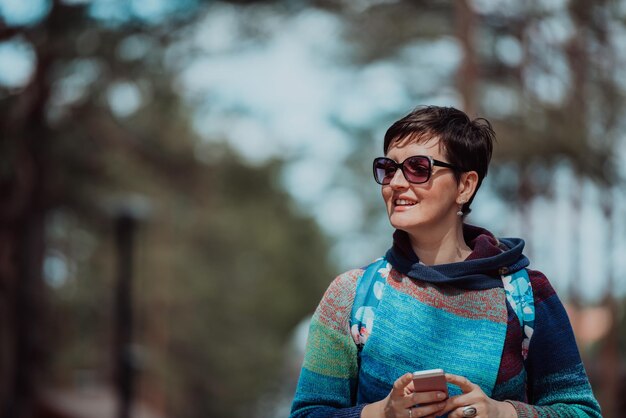 Een vrouw in een modieuze outfit die een smartphone gebruikt terwijl ze op een mooie zonnige dag tijd doorbrengt in het park.