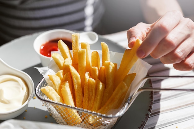 Een vrouw in een restaurant of fastfoodcafé eet gefrituurde vleugels in luchtbeslag met verschillende sauzen en friet