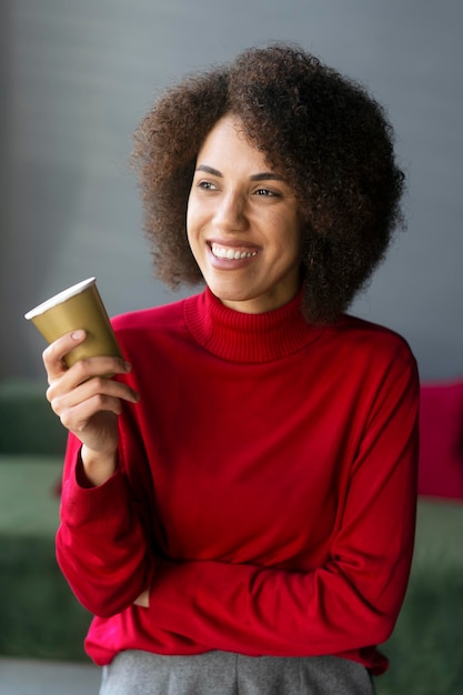 Een vrouw in een rode coltrui houdt een kopje koffie vast