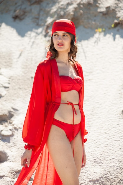 Een vrouw in een rode outfit staat in het zand.