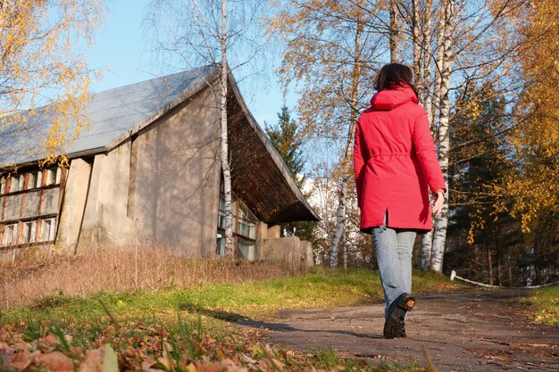 Een vrouw in een rood jasje loopt door het herfstpark tussen de gele gevallen bladeren