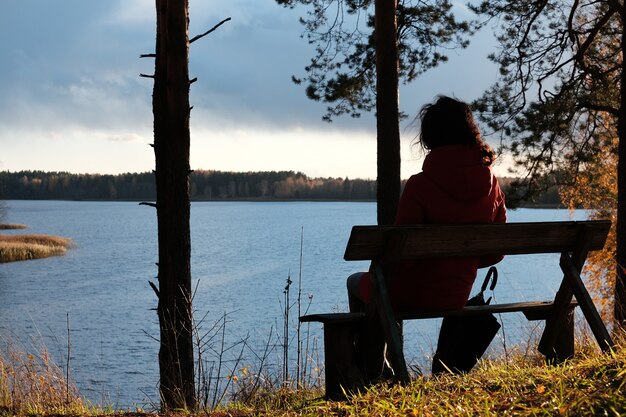 Een vrouw in een rood jasje zit op een bankje in het park