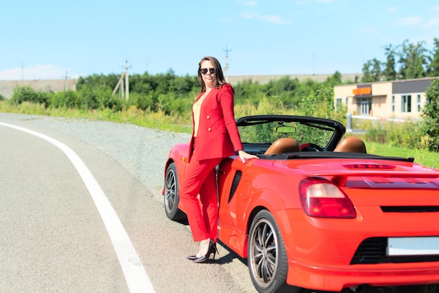 Een vrouw in een rood pak staat naast een rode sportwagen.