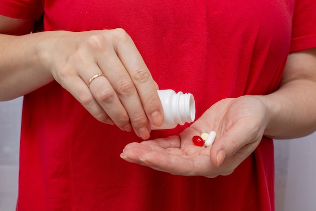 Een vrouw in een rood t-shirt houdt een fles pillen vast en giet medicijnen in haar handpalm