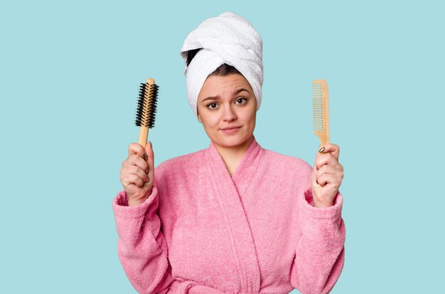 Een vrouw in een roze badjas met een haarborstel en kam met een handdoek om haar hoofd gewikkeld