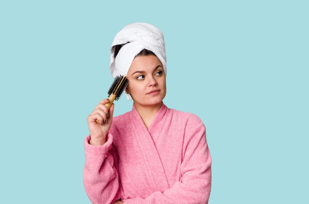 Een vrouw in een roze badjas met een haarborstel en kam met een handdoek om haar hoofd gewikkeld