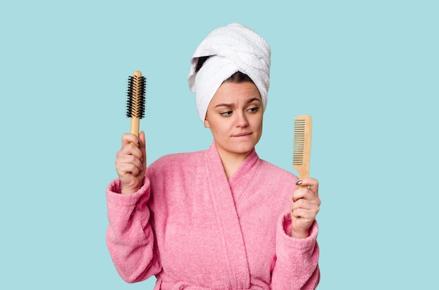 Een vrouw in een roze badjas met een haarborstel en kam met een handdoek om haar hoofd gewikkeld