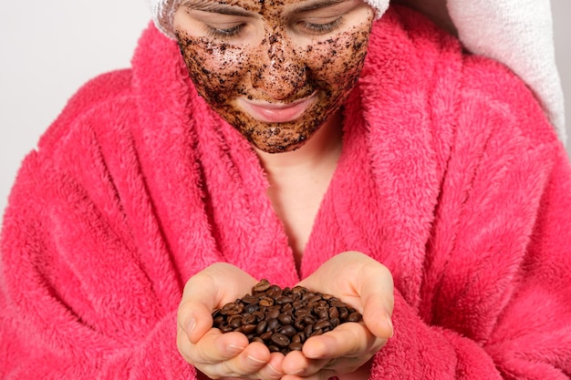 Een vrouw in een roze badjas met een koffiemasker op haar gezicht