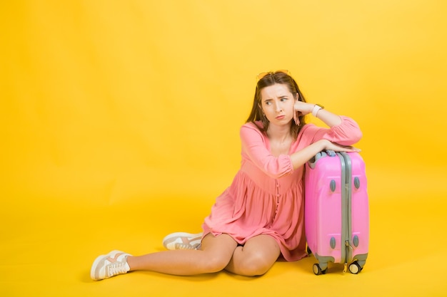 Een vrouw in een roze jurk houdt een grote roze koffer met bagage in haar handen