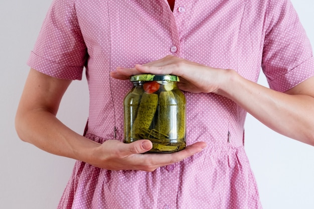 Een vrouw in een roze jurk houdt een pot augurken vast. Bewaartijd, herfstoogst, verse boerderijproducten