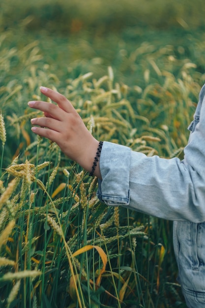 Een vrouw in een spijkerjasje raakt de groene korenaren aan met haar hand 1