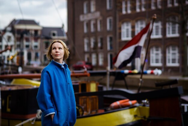 Een vrouw in een stijlvolle blauwe jas op een kanaal met schepen en een wapperende vlag van Frankrijk Gevoelens van passie voor reizen en avontuur Woonwijk in Nederland