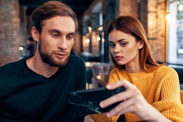 Een vrouw in een trui met een mobiele telefoon en een man met een baard zitten in een restaurant