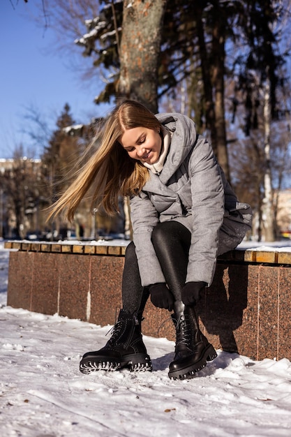 Een vrouw in een winterdonsjack en leren laarzen loopt door een besneeuwde straat leren winterschoenen voor dames