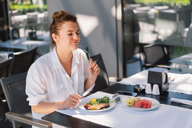 Een vrouw in een wit hemd eet lunch of ontbijt buiten in een café